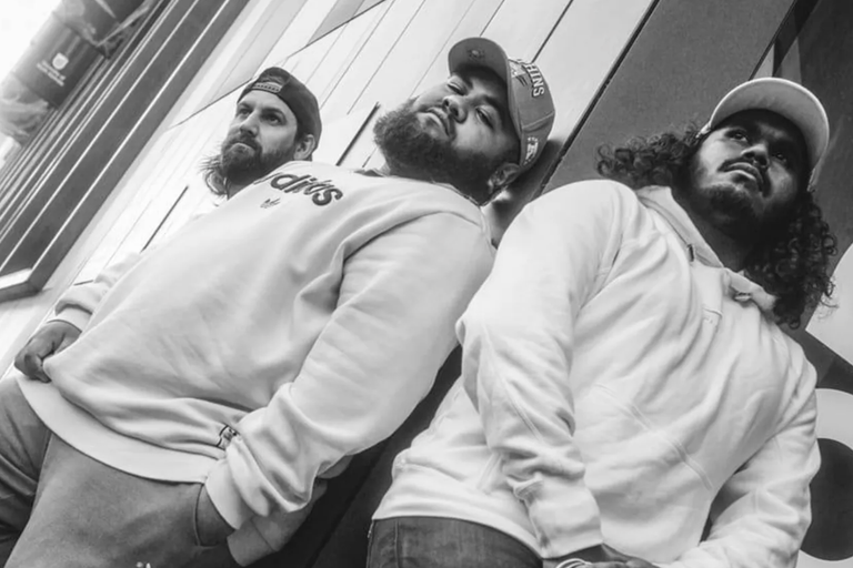 First Nations hip-hop group DEM MOB posing outdoors in hoodies and caps for a low-angle black-and-white promotional artist portrait photo shoot.